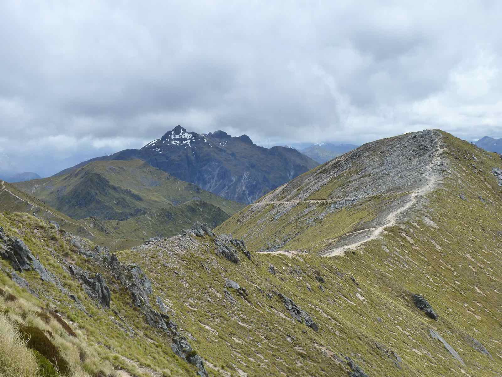 A track running along a grassy alpine ridge towards distant peaks