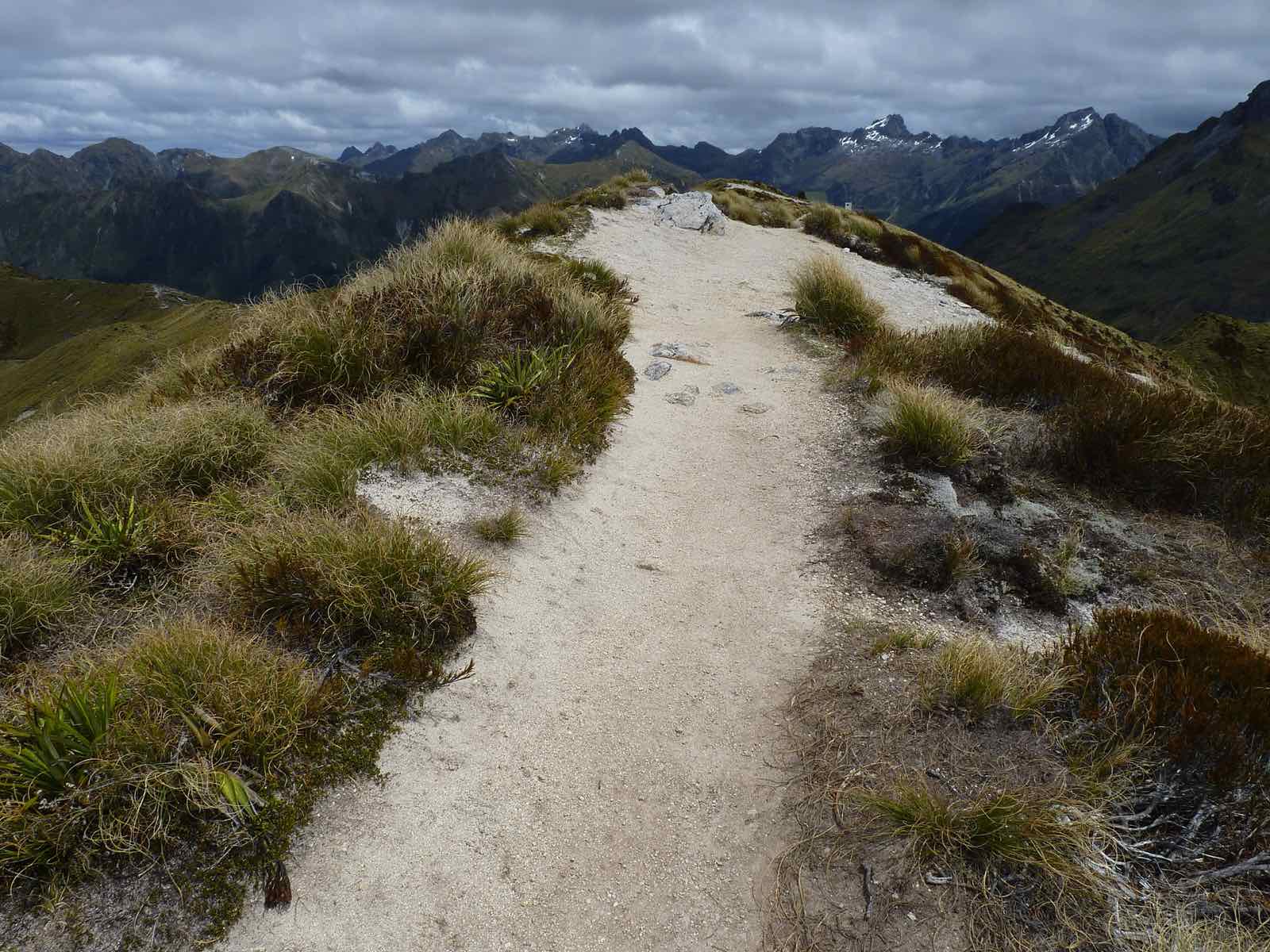 A wide gravel path along a tussock ridge with dark mountains behind