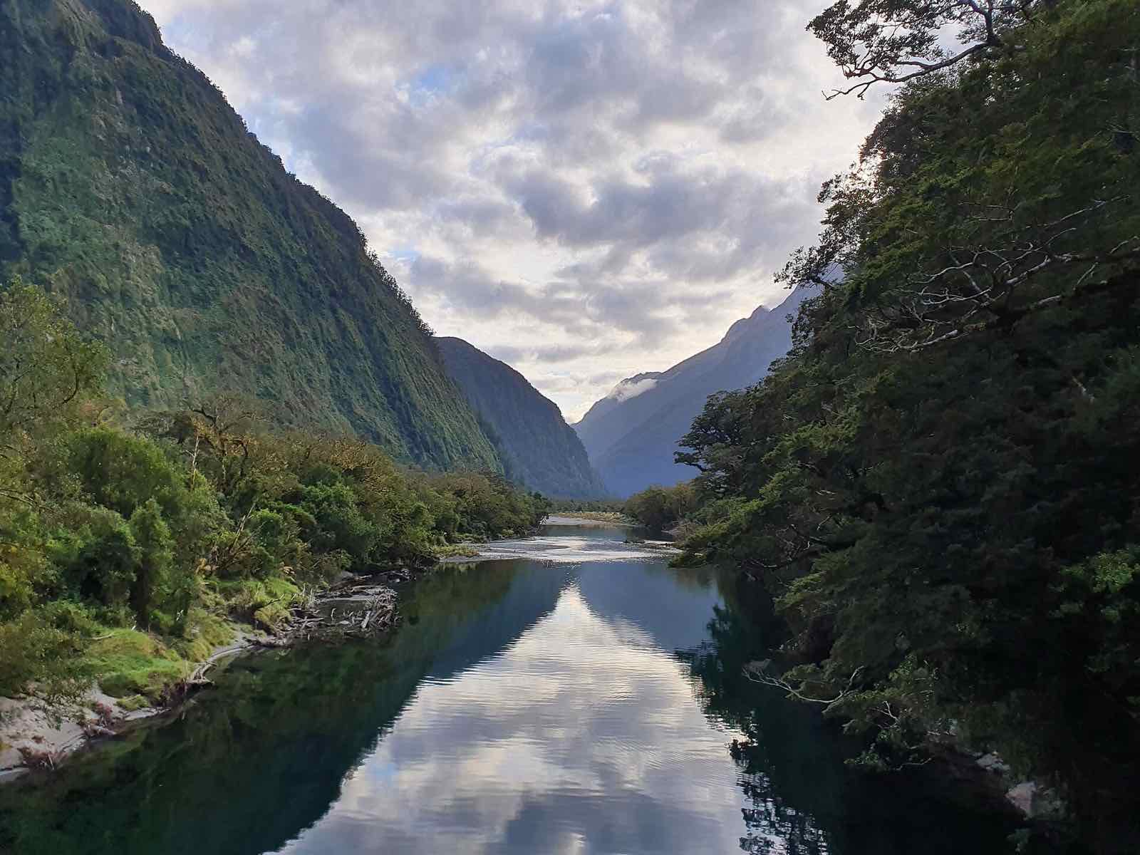 The still Arthur River reflecting the sky between steep forested valley walls