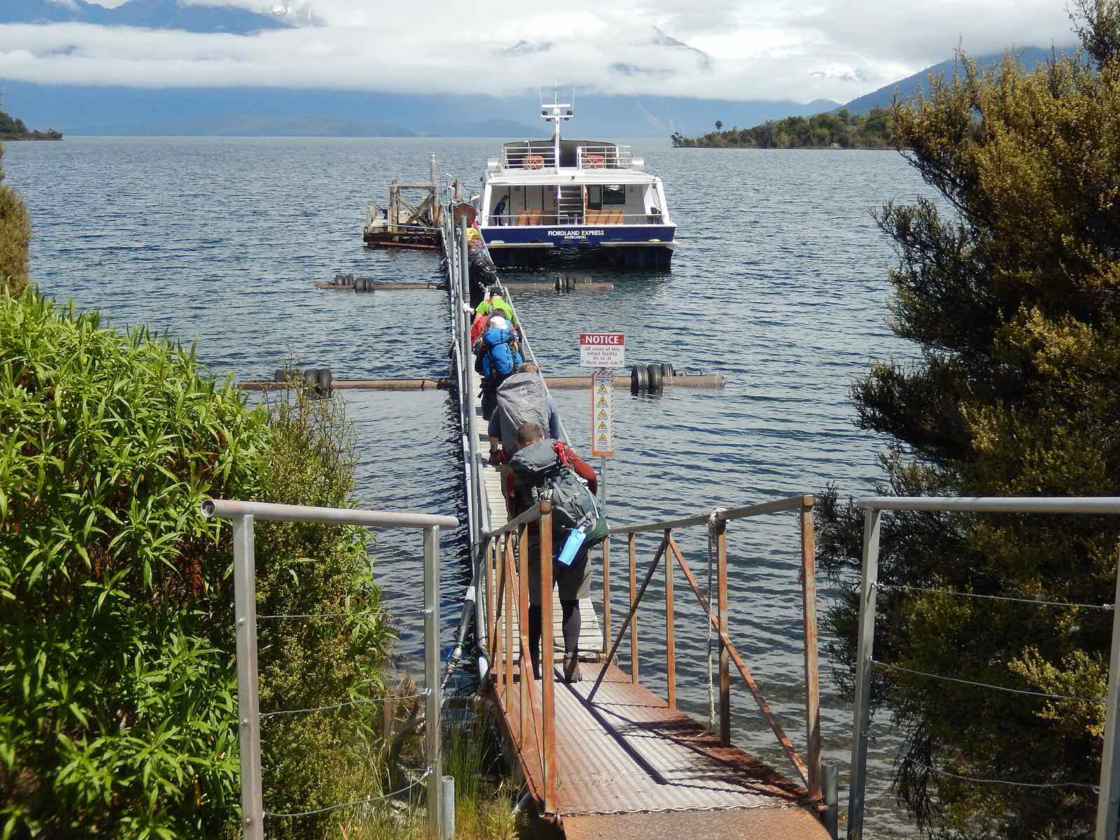 Trampers with packs walking down a jetty to a boat on Lake Te Anau